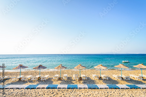 Fototapeta Naklejka Na Ścianę i Meble -  Beaches, Greece, Kos Island, Kardamena: beautiful holiday setting on a secluded beach with umbrellas on the Greek Aegean Sea with turquoise waters and a picturesque bay and islands in the background