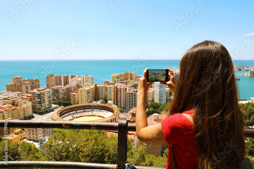 Beautiful girl with mobile phone take picture of Malaga landscape with bullring, Malaga, Spain photo