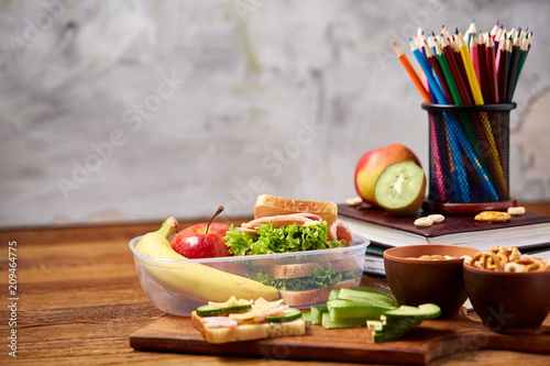 Obraz na plátne School or picnic lunch box with sandwich and various colorful vegetables and fruits on wooden background, close up