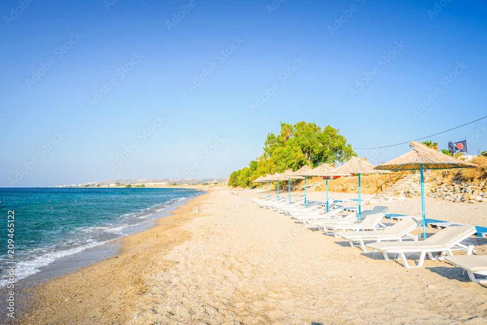 Beaches, Greece, Kos Island, Kardamena: beautiful holiday setting on a secluded beach with umbrellas on the Greek Aegean Sea with turquoise waters and a picturesque bay and islands in the background