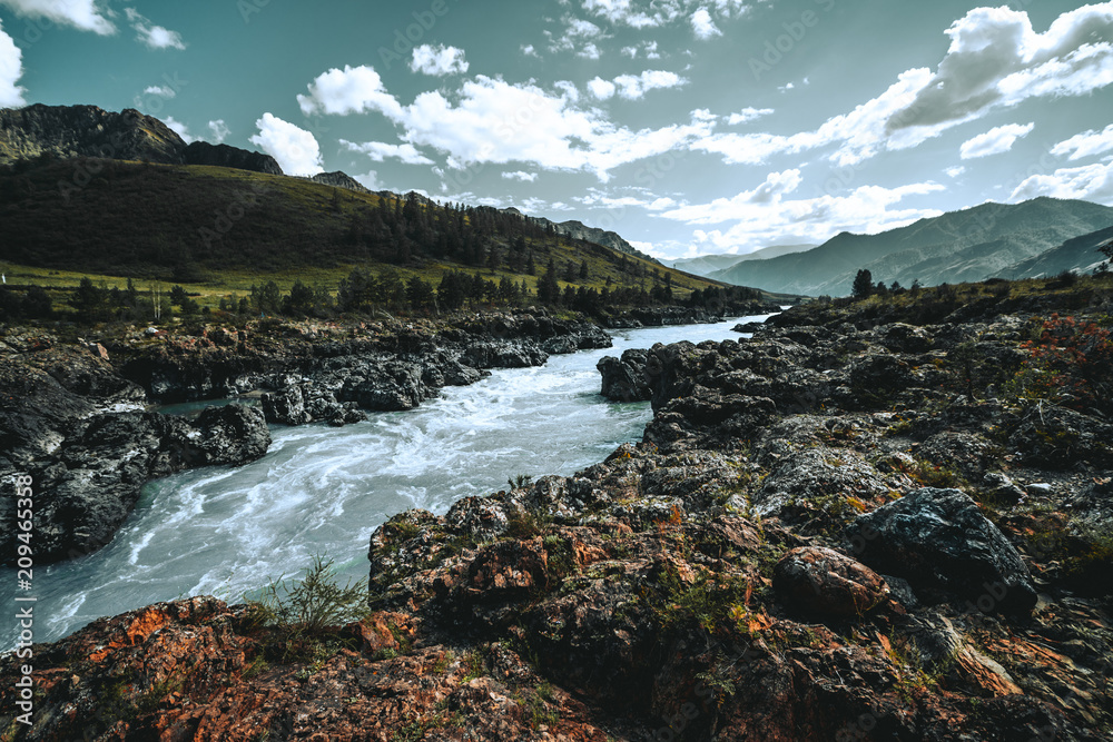 Obraz premium Wide-angle shot of a cliffy contrast mountain riverside overgrown with moss and native grasses, with hills range and meadows around; hazy morning, Altai mountains, Kuyus district, Russia