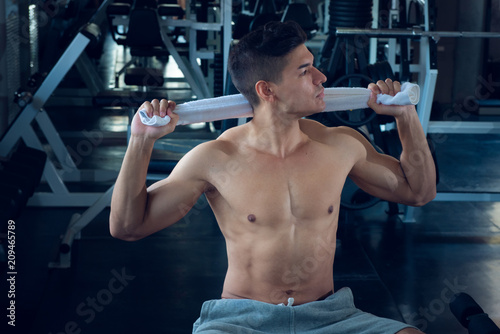 Portrait of sport young fitness man with white towel on his neck, relax after exercise at indoor sport gym, healthy sport concept.