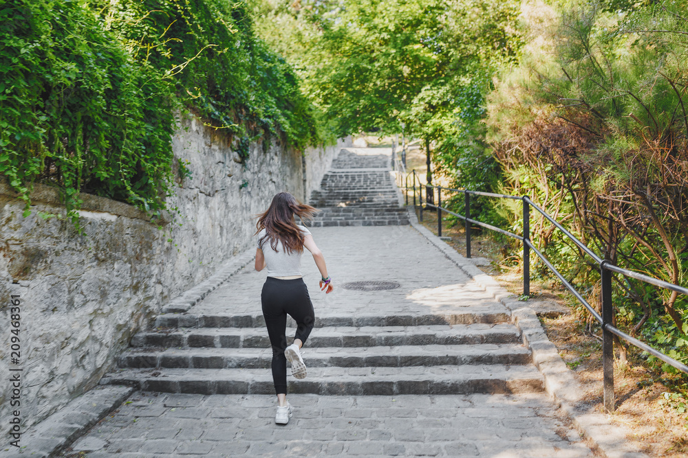 Athletic and fit unrecognizable woman running in the park up the stairs