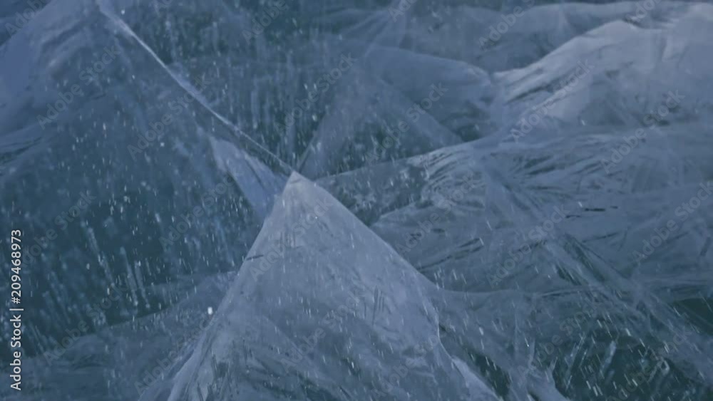 Snow is flying over surface of ice. Snowflakes fly on ice of Lake Baikal. Ice is very beautiful with unusual unique cracks. Snow sparkles and glows in red. Shooting slow motion 180fps. Picture at Snow is flying over surface of ice. Snowflakes fly on ice of Lake Baikal. Ice is very beautiful with unusual unique cracks. Snow sparkles and glows in red. Shooting slow motion 180fps. Picture at
