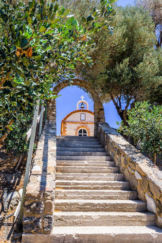 Fototapeta Naklejka Na Ścianę i Meble -  Church, Greece, Kos Island: old cozy little orange stone church with red roof chapel in traditional colors which perched on the greeksy sea next to a small tree over the barren mountains