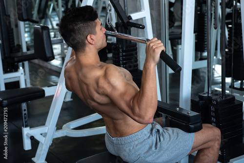 Portrait of young man using weight lifting equipment to build a massive chest and arm at indoor sport gym , bodybuilder concept.