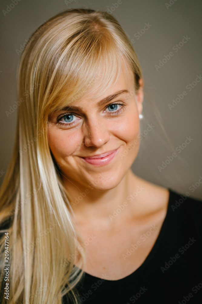 Naklejka premium Close-up profile portrait of a young and attractive blonde woman with blue eyes. She is smiling as she strikes a pose in front of the camera.