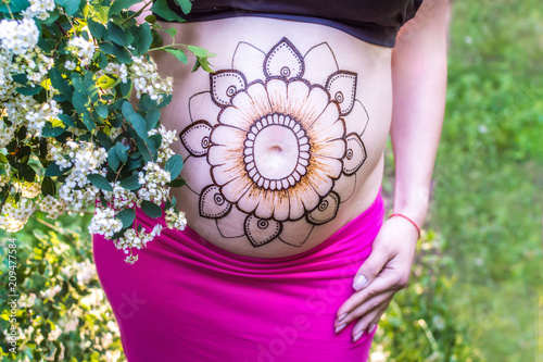 close-up of the belly of a pregnant woman with a mehendi on her stomach against a background of flowers. concept Indian traditions photo