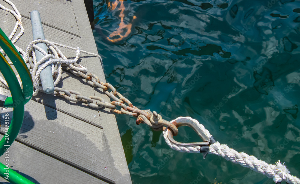 Fototapeta premium Chain attached to cleat on dock and dock tie up that is attached to a boat off camera - shown over deep water