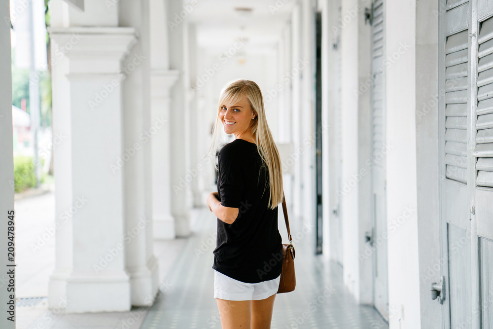 Portrait of a young and attractive blonde woman smiling and standing in an old colonial style building corridor during the day. She is an exchange student to Asia.