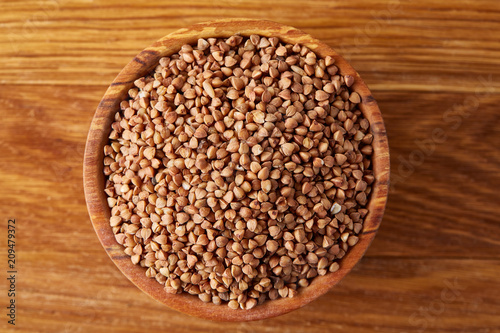 Bowl full of buckwheat grains on rustic wooden table, close-up, selective focus, shallow depth of field. © Aleksey