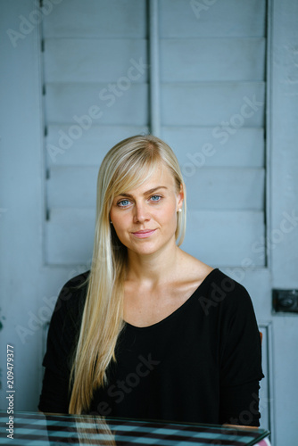 A close-up portrait of a young and attractive blond woman with blue eyes. She is smiling playfully at the camera. 