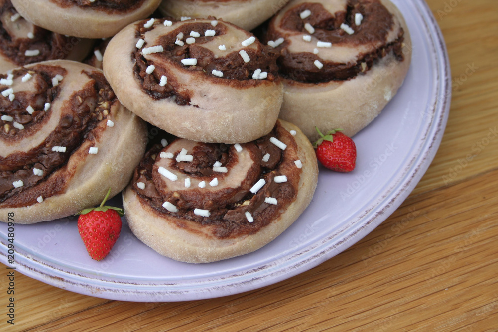 Chocolate rolls on a plate with fresh strawberries on wooden table Chocolate rolls on a plate with fresh strawberries on wooden table