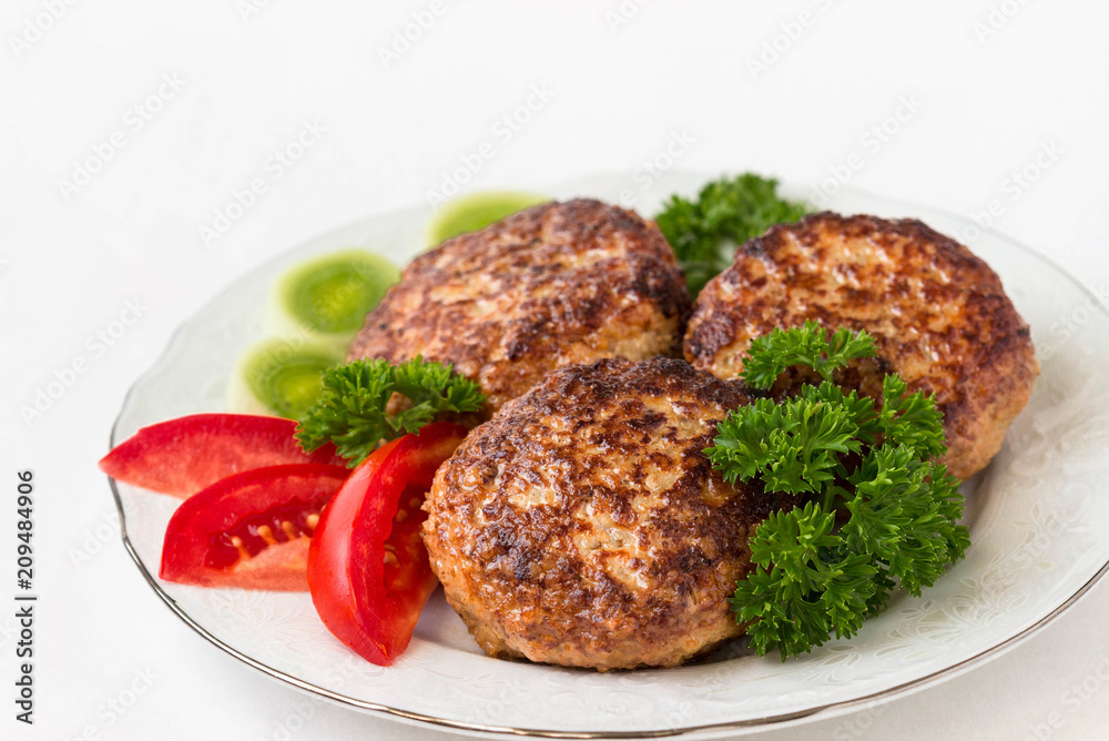 Homemade cutlets with parsley and tomatoes on a white plate and white background. Homemade cutlets with parsley and tomatoes on a white plate and white background.