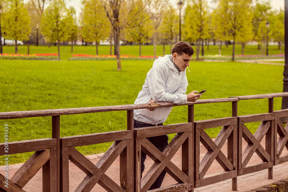 Молодой парень стоит на мосту, мужчина смотрит в телефон и читает сообщение