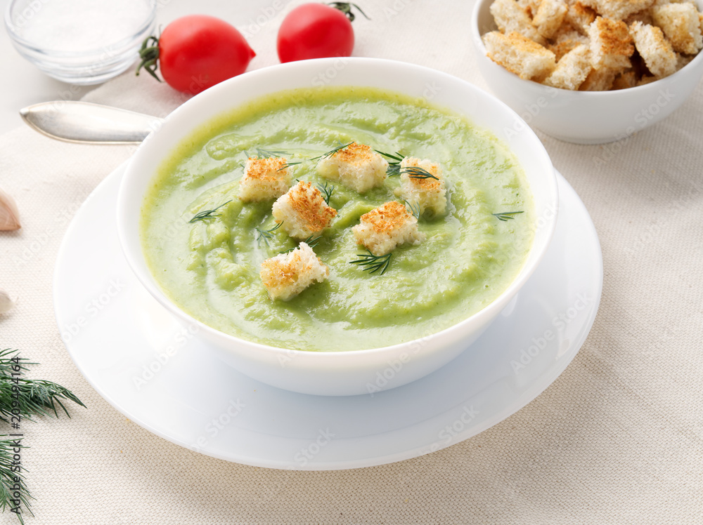 large white bowl with vegetable green cream soup of broccoli, zucchini, green peas on white background, side view