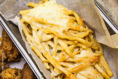 Flat lay above served fast food. French fries in the paper box. Fried potatoes with melted cheese on the top. Unhealthy fast food meals. Delicious meal prepared with cheese.