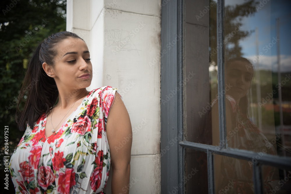 young beautiful woman in colorful dress looking at her reflection in window young beautiful woman in colorful dress looking at her reflection in window