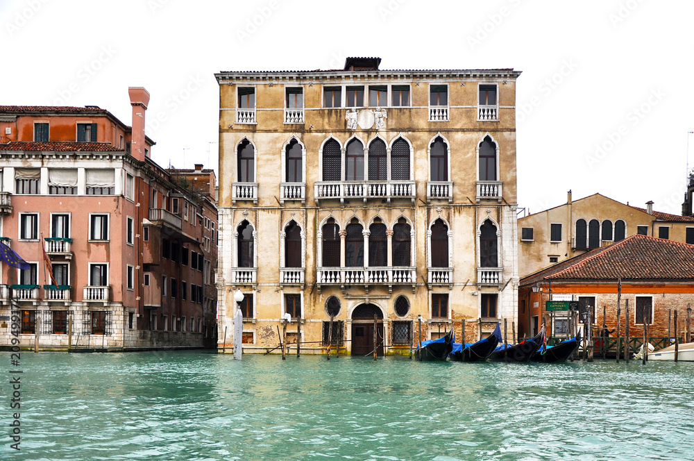 Front view of Gothic building facade on The Grand Canal with a row of blue Gondolas, Venice, Italy.