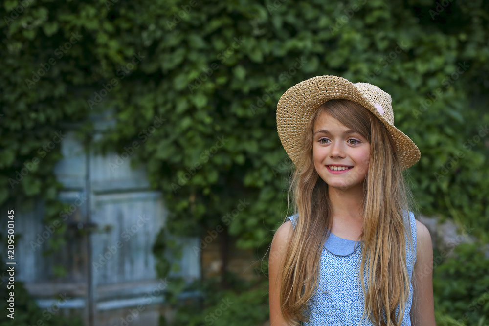 Portrait happy summer mood of joyful young girl in straw hat near blue door in green garden, having fun.positivity, joy, happiness, smiling