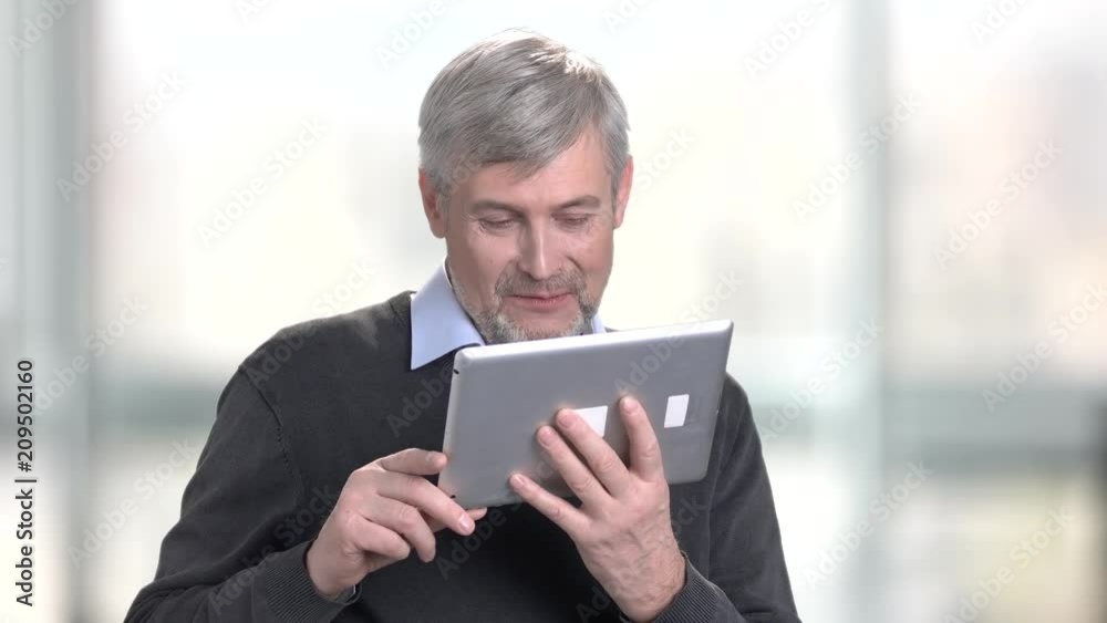 Smiling caucasian man talking via internet. Portrait of friendly mature using computer tablet on blurred background. Smiling caucasian man talking via internet. Portrait of friendly mature using computer tablet on blurred background.