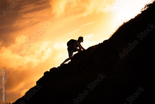 Man hiker climbing up a steep mountain cliff.  People taking risk, motivation and outdoor adventure concept. 