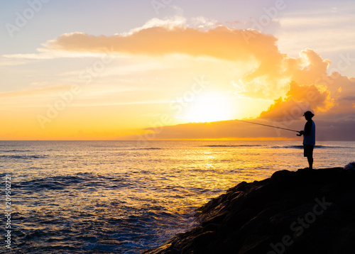 Man fishing by the sea at sunset.