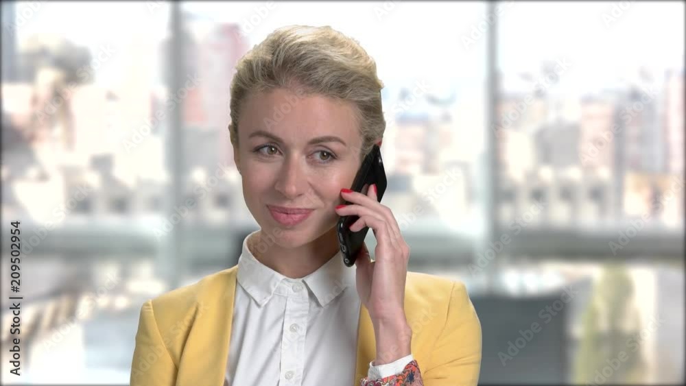 Young pretty business lady talking on smartphone. Young confident woman in formal wear talking on phone on window city background.