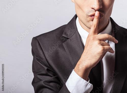 Man saying hush be quiet with finger on lips gesture isolated on gray wall background. Top secret concept.