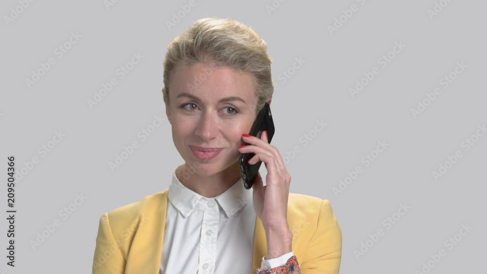 Pretty business woman talking on smartphone. Portrait of beautiful business lady speaking on mobile phone on grey background. Pretty business woman talking on smartphone. Portrait of beautiful business lady speaking on mobile phone on grey background.