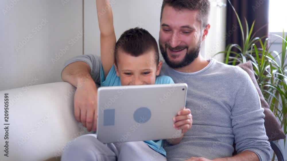 Smiling father and son using tablet while sitting on sofa Smiling father and son using tablet while sitting on sofa