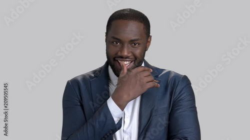 Handsome macho-man on grey background. Portrait of afro-american businessman is winking with eye and smiling.