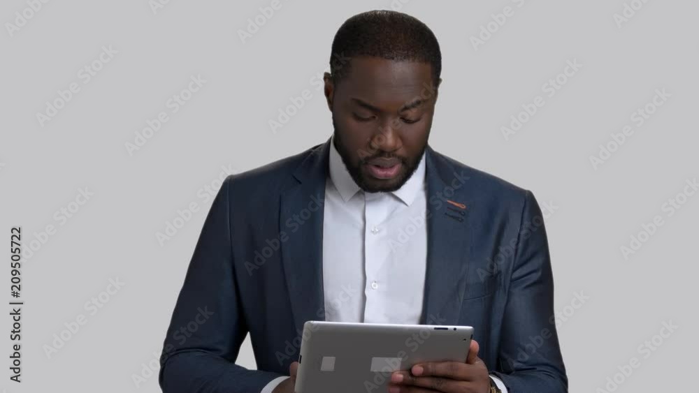 Confident businessman speaking on grey background. Handsome afro-american man in formal wear using computer tablet and talking. Manager talking at conference. Confident businessman speaking on grey background. Handsome afro-american man in formal wear using computer tablet and talking. Manager talking at conference.