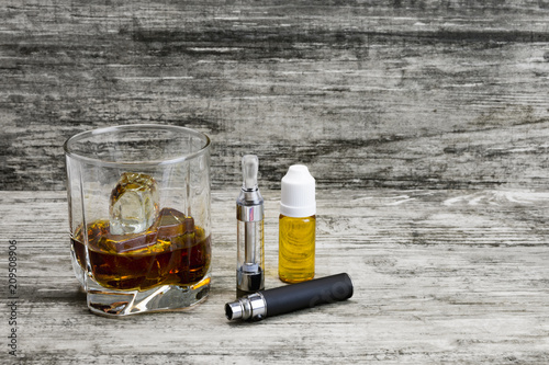 Whiskey in a glass with an e-cigarette and liquid for it on a gray stone background 
 