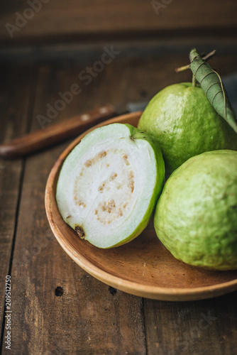 Fresh guava fruit in a wooden bowl and on a wooden background.