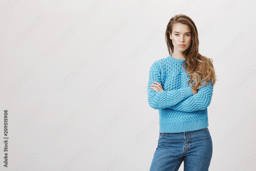 Portrait of attractive woman with poker face standing with crossed hands  and being in bad mood,