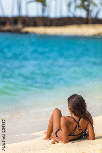 Beach vacation woman lying down on white sand sun tanning at hawaiian holiday travel getaway.