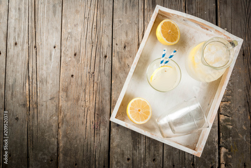 Classic sour and sweet homemade lemonade drink, summer cold iced beverage, rustic wooden background copy space in white tray above