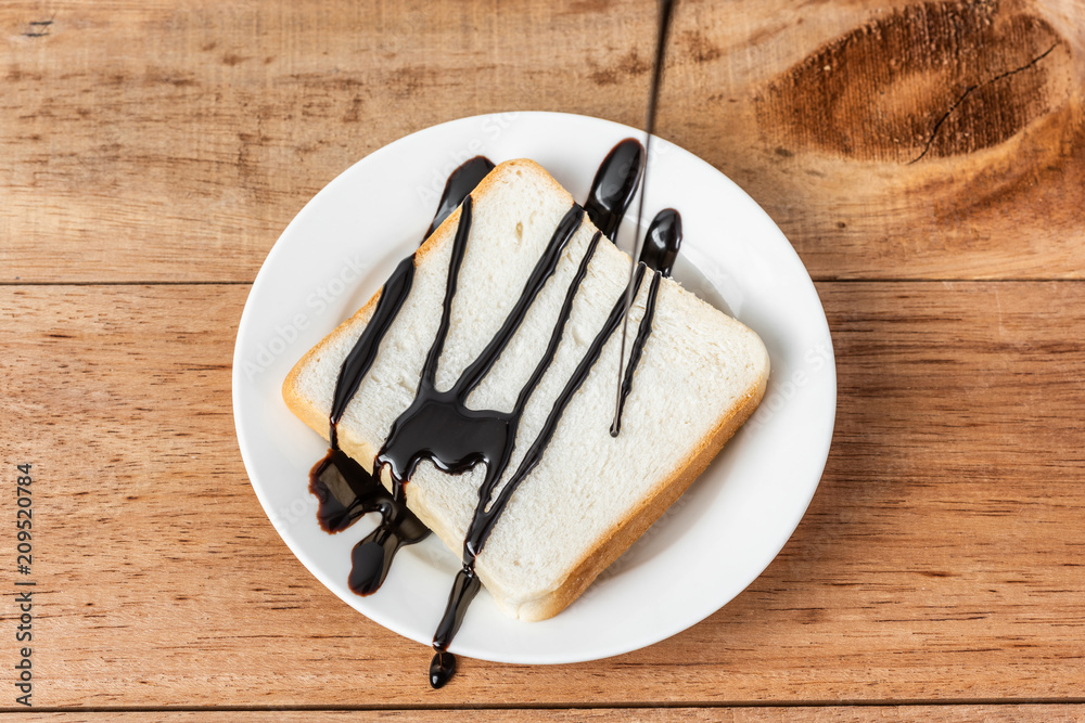 Fototapeta premium chocolate syrup on white sliced bread on dish, wooden background