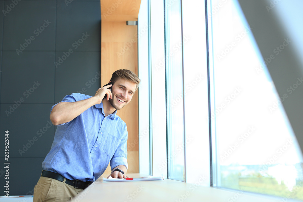 Smiling businessman standing and using mobile phone in office. Smiling businessman standing and using mobile phone in office.