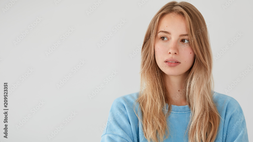 Cute adorable thoughtful young female model looks aside, dressed in loose sweater, has straight hair, isolated over white background with copy space for your advertisement or promotional text. Cute adorable thoughtful young female model looks aside, dressed in loose sweater, has straight hair, isolated over white background with copy space for your advertisement or promotional text.