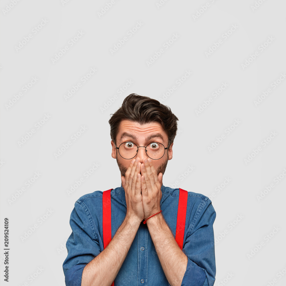Stupefied handsome male stares at camera and covers mouth, has surprised look, sees high price on desirable thing at shop, has not enough money as recieves low salary. People and reaction concept Stupefied handsome male stares at camera and covers mouth, has surprised look, sees high price on desirable thing at shop, has not enough money as recieves low salary. People and reaction concept