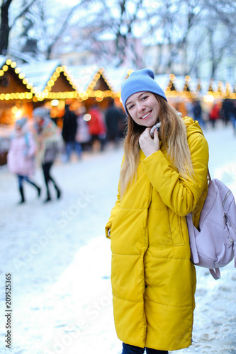 Young girl wearing yellow coat, backpack and cap walking on snow. Concept of fashion and winter season, waiting Christmas. photo