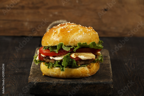 Hamburger on a wooden board against a dark background with copy space. Hamburger with sauce and fresh vegetables on a wooden table. Burger.