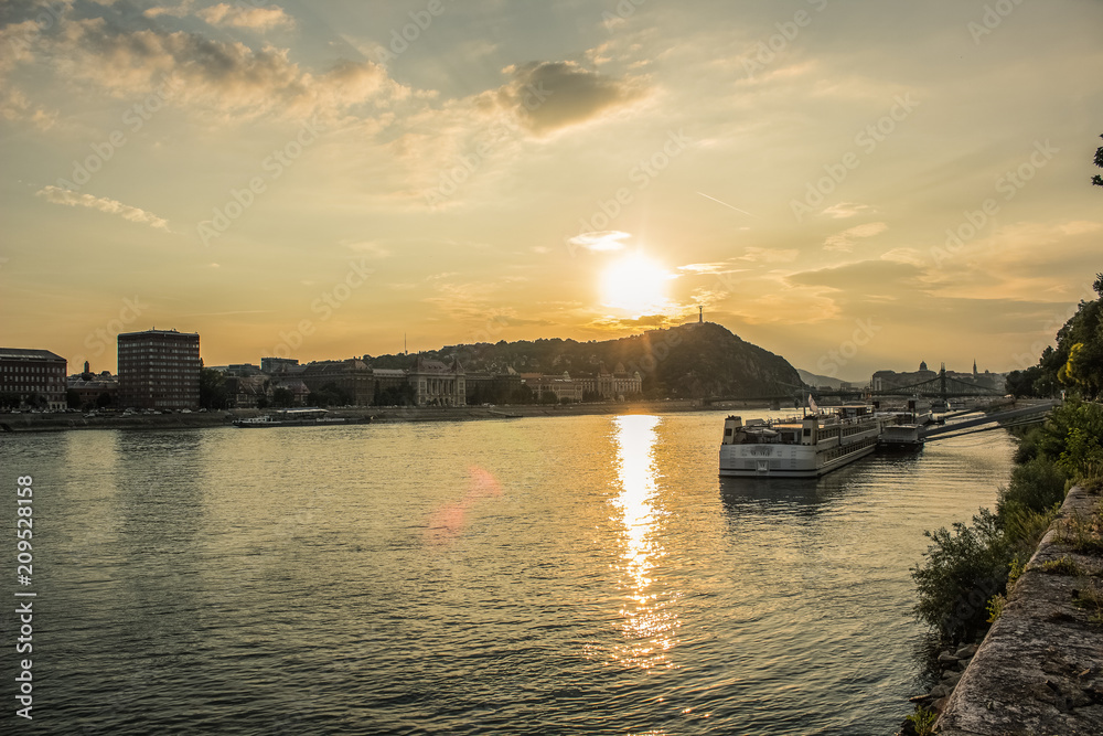 Budapest waterfront urban city scape in sunset time with Danube river ships and sun glares