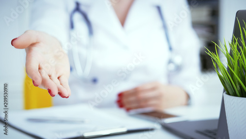 Female doctor making welcome gesture  politely inviting patient to sit down in medical office. Photo with depth of field.