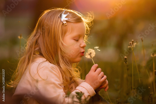 girl blowing fluffy dandelion at sunset