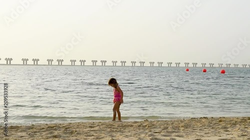 Cute little girl in pink swimming suit playing at the beach in Dubai