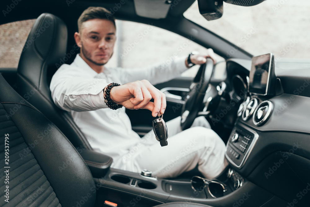 Handsome Young Man Showing Car Keys in His Newly Bought Auto Sitting in the Luxury Vehicle Handsome Young Man Showing Car Keys in His Newly Bought Auto Sitting in the Luxury Vehicle