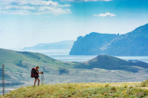 Young woman hiker with backpack and trekking sticks on a hill